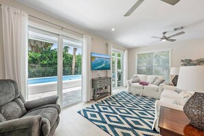 Un soggiorno moderno con vista piscina, una TV a schermo piatto e un ventilatore a soffitto.
