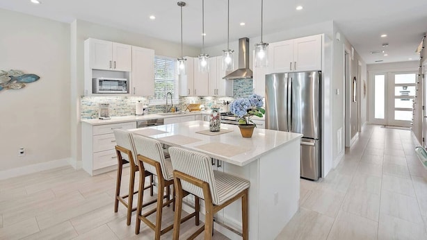 A modern kitchen with white cabinetry, stainless steel appliances, and a central island with bar stools. - Movie Theater, Heated Pool, & Sauna - Luxe 4BR (West Palm Beach)