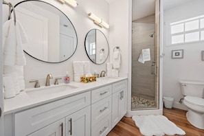 A modern bathroom with a white vanity, two large mirrors, a glass shower enclosure, and a white toilet. - Movie Theater, Heated Pool, & Sauna - Luxe 4BR (West Palm Beach)