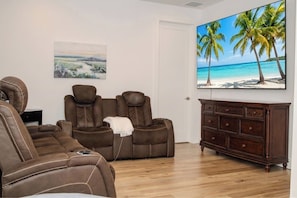 A living room with a brown leather sofa, a recliner, a wooden cabinet, and a painting of a beach scene. - Movie Theater, Heated Pool, & Sauna - Luxe 4BR (West Palm Beach)
