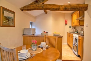 A cozy kitchen with wooden cabinets, a built-in oven, and a dining area with a wooden table set for two.