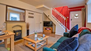 A cozy living room with a fireplace, a television, a staircase with red railings, and a comfortable sofa.