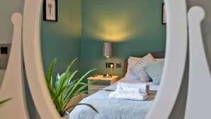 Ein Schlafzimmer mit einem Bett, einem Nachttisch, einer Lampe und einem gerahmten Bild an der Wand.