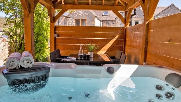 Ein Whirlpool unter einer Hollaube mit einem Tisch und Stühlen in der Nähe.