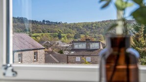 A view from a window overlooking a rural landscape with stone buildings and a hill in the distance. - Beech Cottage - Central Luxury (Derbyshire)