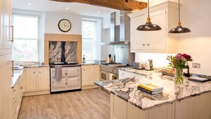 Una cocina moderna con armarios blancos, una isla de mármol, horno empotrado e iluminación colgante.