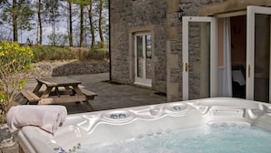 Un edificio de piedra con un jacuzzi, una mesa de picnic de madera y una puerta que da a una habitación.