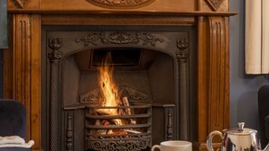 Una chimenea encendida, una mesa con dos tazas blancas y un hervidor plateado.