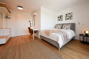Een slaapkamer met een bed, een bureau, een stoel, een spiegel en een nachtkastje met een lamp.