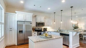 A modern kitchen with white cabinetry, stainless steel appliances, and a granite countertop island.