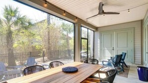 A covered patio with a wooden table and chairs, a ceiling fan, and a view of trees and a fence.