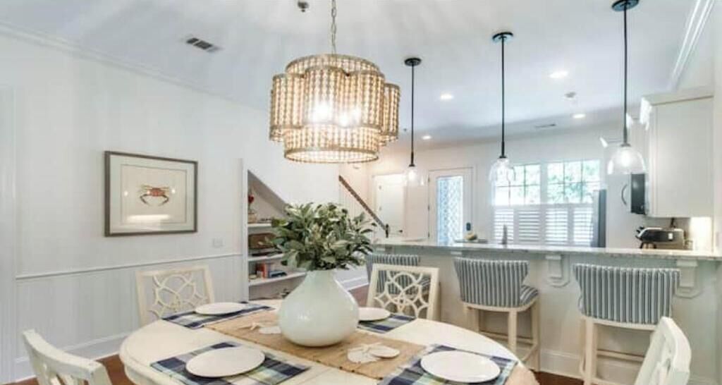 Un coin repas avec une table dressée pour quatre personnes, un lustre et une vue sur la cuisine.