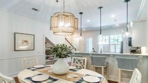 A dining area with a table set for four, a chandelier, and a view of the kitchen.