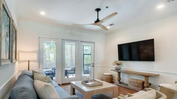 A spacious living room with a sofa, coffee table, and a television mounted on the wall.