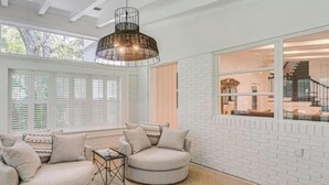 A cozy living room with a round sofa, a coffee table, and a large window with shutters. - A Little Gem - Ocean Views with Private Elevator (Jekyll Island)