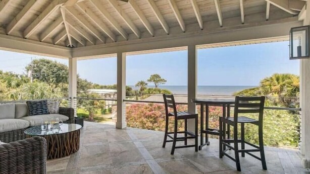 A covered patio with a view of the ocean, furnished with a sofa, chairs, and a table. - A Little Gem - Ocean Views with Private Elevator (Jekyll Island)