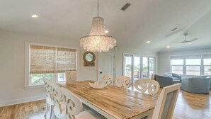 A spacious living room with a wooden dining table, white chairs, and a chandelier. - A Little Gem - Ocean Views with Private Elevator (Jekyll Island)