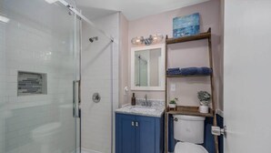 Un bagno con cabina doccia in vetro, un water bianco e un mobile lavabo blu con piano in marmo.