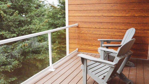 En træterrasse med hvid gelænder, en grå Adirondack-stol og udsigt til et skovområde.