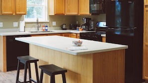 A modern kitchen with wooden cabinets, a central island with stools, a black refrigerator, and a microwave.