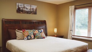 A neatly made bed with a patterned pillow, a wooden headboard, a bedside lamp, and a window with curtains.