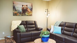 A living room with two dark brown leather sofas, a round wooden coffee table, and a painting of a bear on the wall.