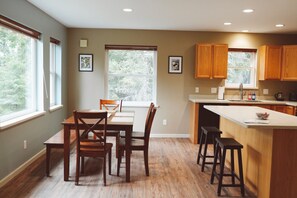 A modern kitchen with wooden cabinets, a dining table with chairs, and a large window providing natural light.