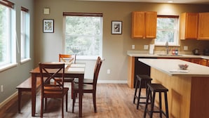 A kitchen with wooden cabinets, a dining table with chairs, a bar counter, and a large window.
