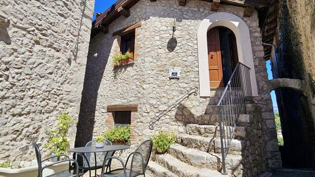 Un edificio de piedra con una puerta de madera, una ventana pequeña con plantas y una escalera que lleva a la entrada.