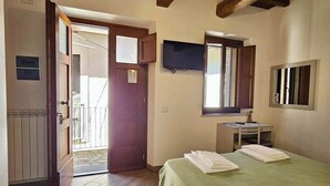Una habitación con techo de madera, cama con ropa de cama verde, escritorio con silla, televisor y puerta que da al exterior.