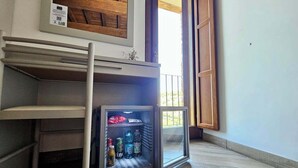 Una habitación compacta con un mini refrigerador integrado que contiene bebidas, una ventana pequeña y techo de madera.