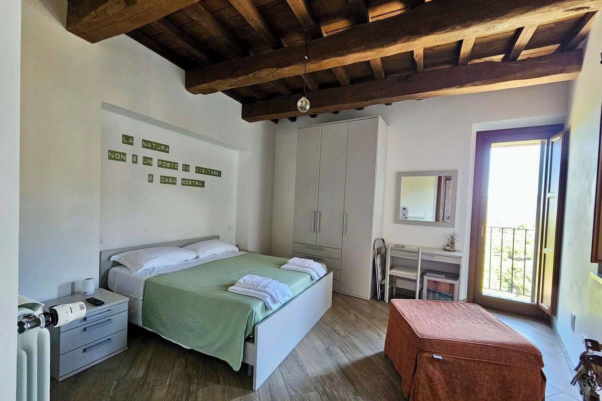 Un dormitorio con cama, escritorio, silla, armario y balcón.