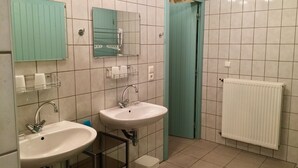 Un baño con dos lavamanos, un espejo, un inodoro y una puerta que da a otra habitación.