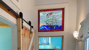 Un pasillo estrecho que conduce a un dormitorio con cama, un armario de madera y un ventanal con vidrieras.