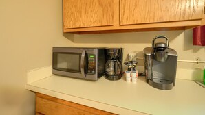 A kitchen with a microwave, coffee maker, and coffee pods on the counter.