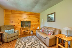 Una sala de estar acogedora con una pared de madera, un sofá de cuero marrón, un sillón marrón, un tapete estampado y una mesita de madera con una lámpara.