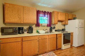 A kitchen with wooden cabinets, a microwave, a coffee maker, a toaster, a sink, a stove, and a refrigerator.