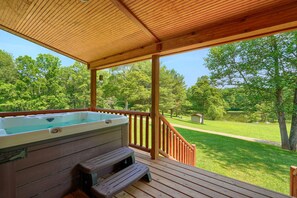 A wooden deck with a hot tub and a bench, overlooking a grassy area with trees.