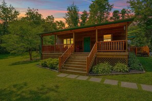 A wooden cabin with a porch, steps, and a green door.