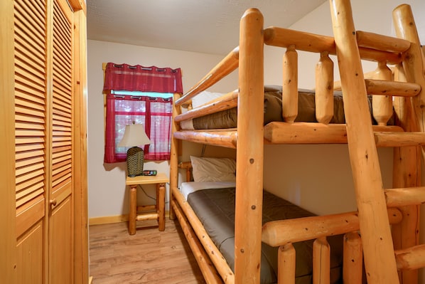 Una cama litera con estructura de madera, un escritorio pequeño con lámpara y una ventana con cortina roja.