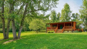 A wooden cabin with a porch, surrounded by lush green grass and trees.