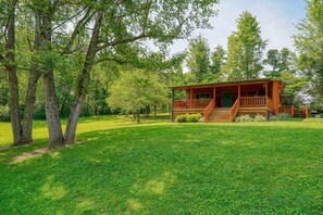 A wooden cabin with a porch, surrounded by lush green grass and trees.