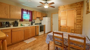 A compact kitchen with wooden cabinets, a refrigerator, a stove, and a dining table with chairs.