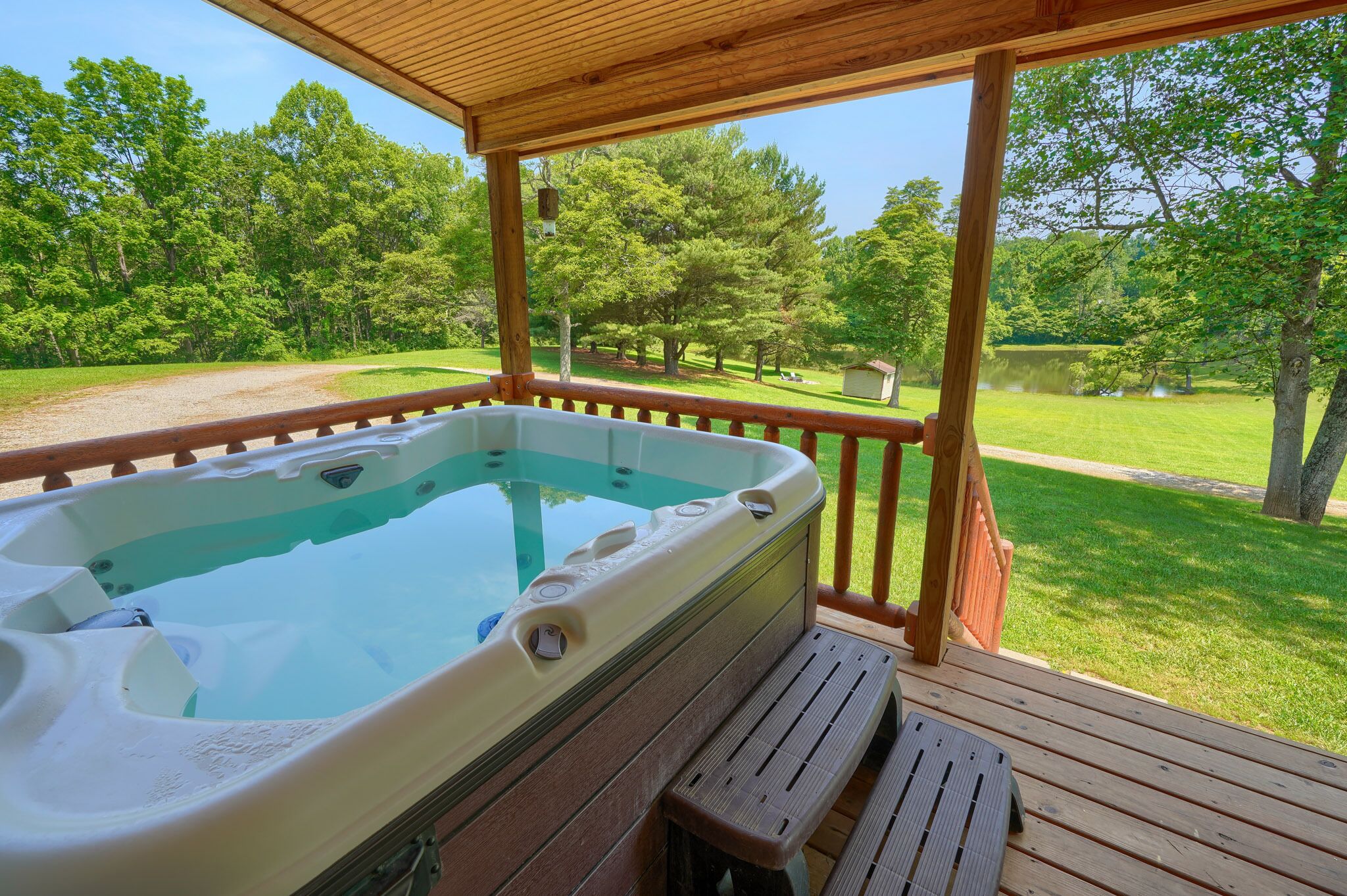 A hot tub on a wooden deck with a view of a grassy area and trees.