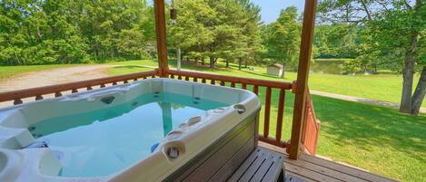 A hot tub on a wooden deck with a view of a grassy area and trees.