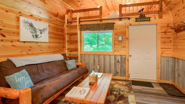 Un acogedor interior de cabaña con detalles de madera, un sofá de cuero marrón, una mesa de centro de madera y un ventanal con vistas a árboles verdes.