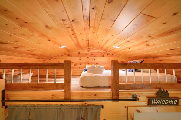 A cabin with a wooden ceiling, a bed with white bedding, and a 'Welcome' sign.