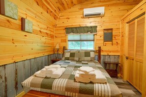 Une chambre dans une cabane en bois, avec un lit, deux tables de chevet, une fenêtre et une porte.