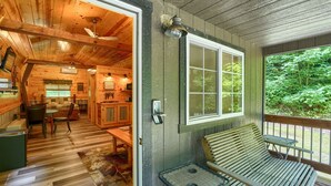 Interior de una cabaña de madera con comedor, banco y vista al exterior.