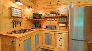 Cocina de cabaña de madera con estufa a gas, microondas, refrigerador y varios utensilios de cocina.